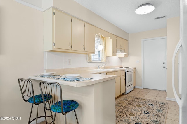 kitchen featuring cream cabinetry, a breakfast bar, white appliances, and light tile patterned floors