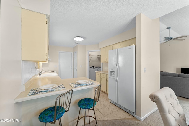 kitchen with ceiling fan, light tile patterned flooring, cream cabinetry, white fridge with ice dispenser, and washing machine and dryer