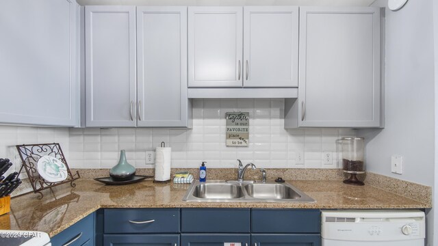 kitchen with tasteful backsplash, blue cabinetry, light stone counters, white dishwasher, and sink