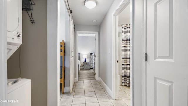 hallway featuring baseboards, stacked washer and clothes dryer, and light tile patterned flooring