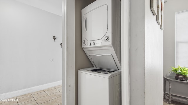 laundry room featuring baseboards, light tile patterned floors, stacked washer and dryer, and laundry area