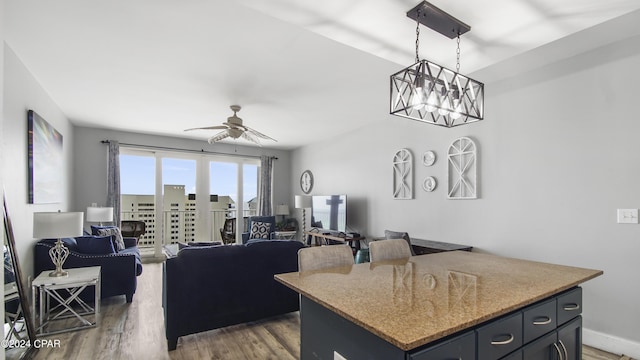 kitchen with pendant lighting, light stone countertops, a ceiling fan, a center island, and wood finished floors