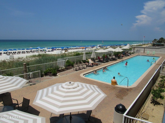 view of swimming pool with a water view, a view of the beach, and a patio area