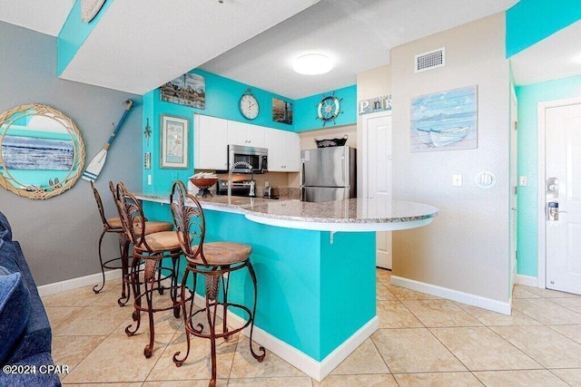 kitchen featuring light stone counters, stainless steel appliances, kitchen peninsula, white cabinets, and a breakfast bar area