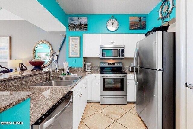 kitchen with appliances with stainless steel finishes, light tile patterned floors, sink, and white cabinetry