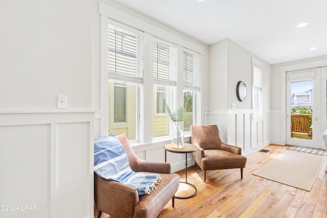 sitting room featuring wainscoting, a decorative wall, light wood-type flooring, and a healthy amount of sunlight