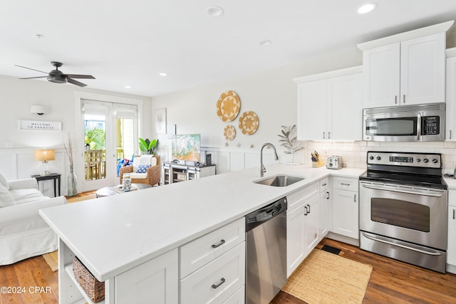 kitchen with light countertops, appliances with stainless steel finishes, open floor plan, a sink, and a peninsula