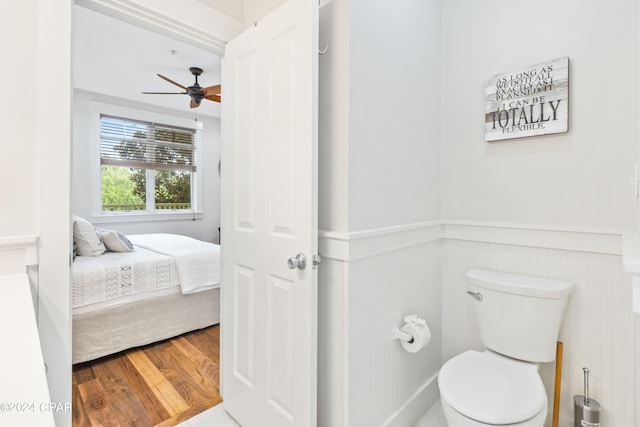 ensuite bathroom with a wainscoted wall, toilet, ensuite bathroom, a ceiling fan, and wood finished floors