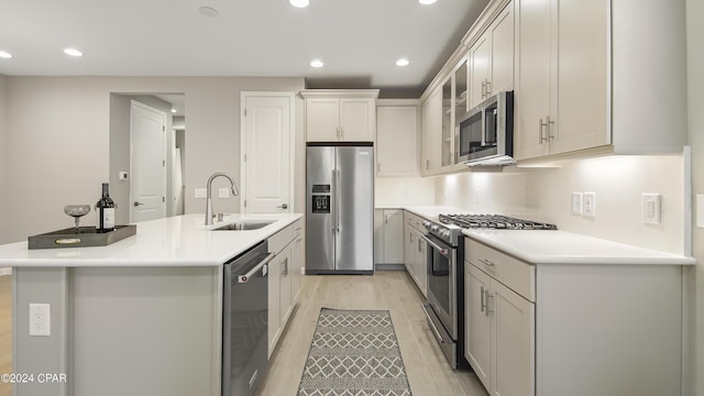 kitchen featuring high quality appliances, white cabinetry, sink, a center island with sink, and light wood-type flooring