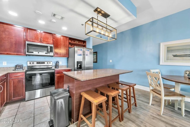 kitchen featuring light stone counters, decorative light fixtures, appliances with stainless steel finishes, a kitchen breakfast bar, and a kitchen island