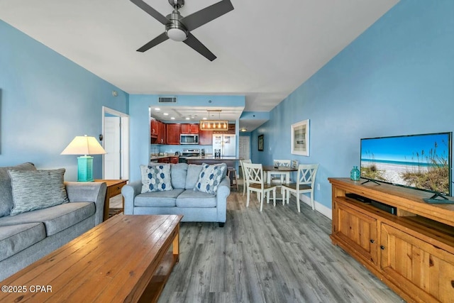 living room featuring ceiling fan with notable chandelier and light hardwood / wood-style flooring