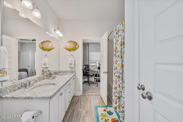 full bath with a sink, a textured ceiling, wood finished floors, ensuite bath, and double vanity