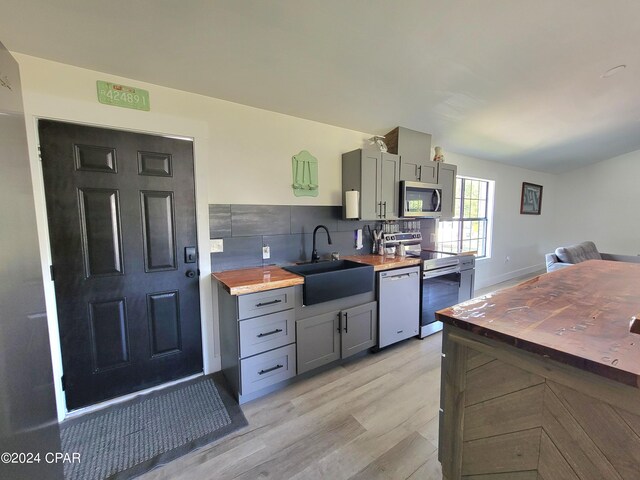 kitchen featuring sink, appliances with stainless steel finishes, light hardwood / wood-style flooring, wood counters, and gray cabinetry