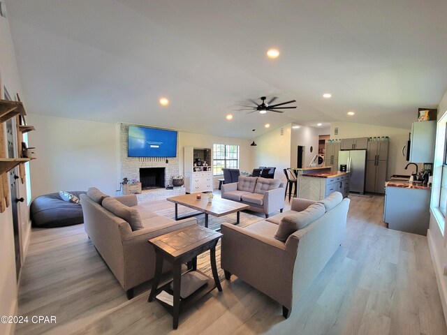 living room with a fireplace, sink, vaulted ceiling, ceiling fan, and light hardwood / wood-style flooring