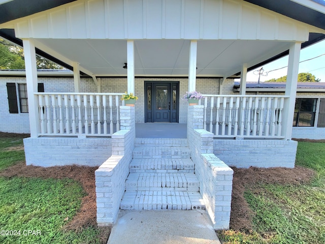 entrance to property with a porch, board and batten siding, and brick siding