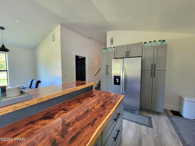 kitchen with wooden counters, pendant lighting, stainless steel refrigerator with ice dispenser, lofted ceiling, and light hardwood / wood-style flooring