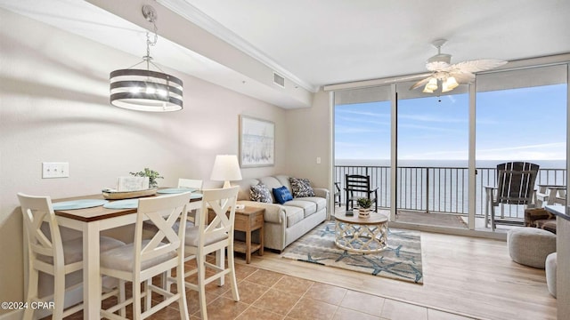 living room featuring floor to ceiling windows, a water view, crown molding, light tile patterned floors, and ceiling fan with notable chandelier