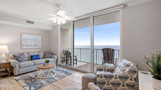 living room featuring floor to ceiling windows, a water view, crown molding, and light hardwood / wood-style flooring