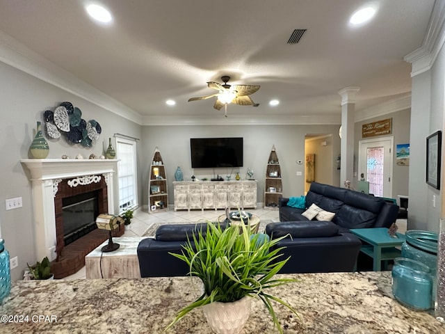 tiled living room with ceiling fan, ornamental molding, a brick fireplace, and ornate columns