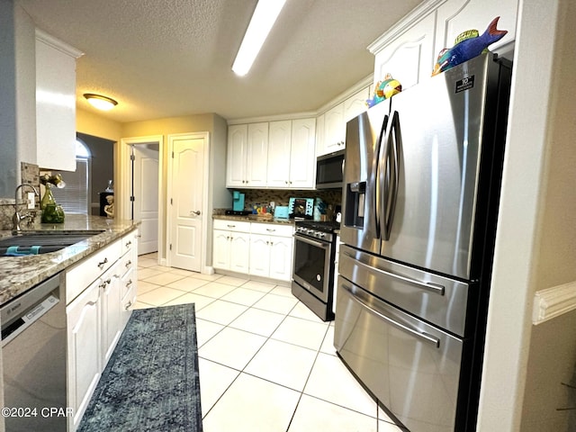 kitchen with dark stone counters, light tile patterned floors, stainless steel appliances, sink, and white cabinets