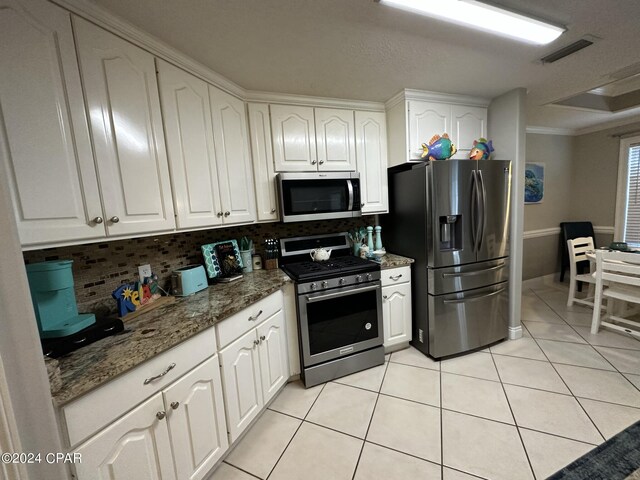 kitchen with backsplash, appliances with stainless steel finishes, ornamental molding, white cabinets, and light tile patterned flooring