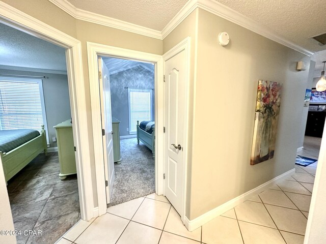 corridor featuring light tile patterned floors, crown molding, and a textured ceiling