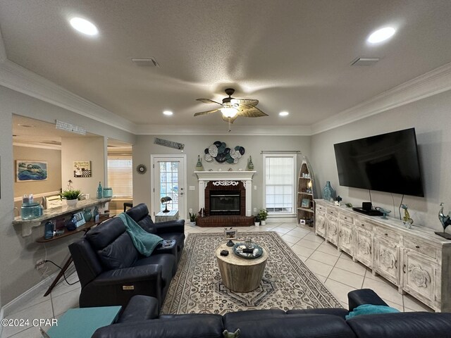 living room with light tile patterned floors, crown molding, a brick fireplace, ceiling fan, and a textured ceiling