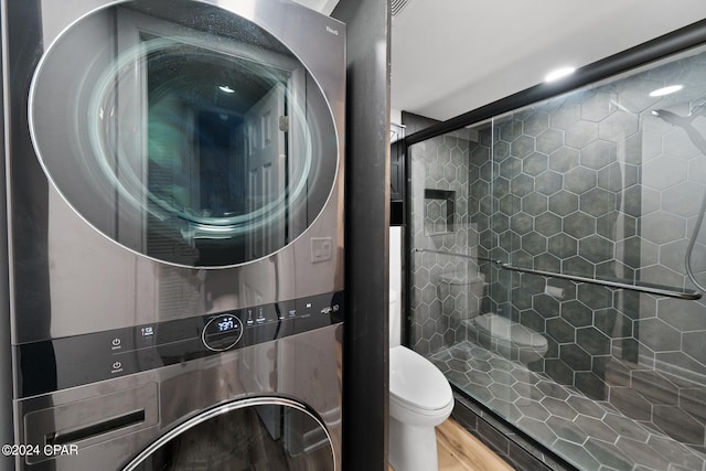 bathroom featuring toilet, wood-type flooring, stacked washer and dryer, and a shower with door