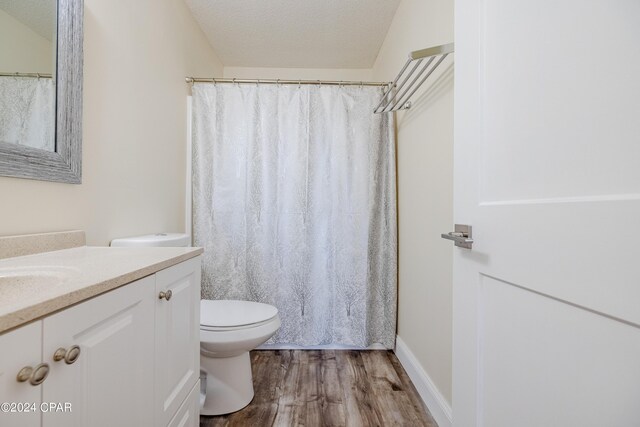 bathroom featuring curtained shower, vanity, a textured ceiling, hardwood / wood-style flooring, and toilet