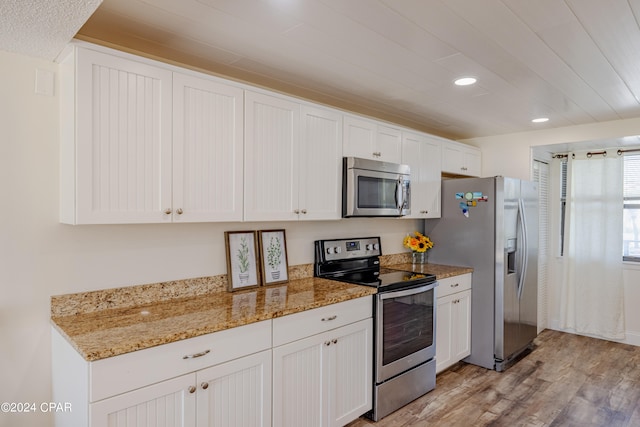 kitchen with light hardwood / wood-style flooring, white cabinetry, appliances with stainless steel finishes, and light stone counters