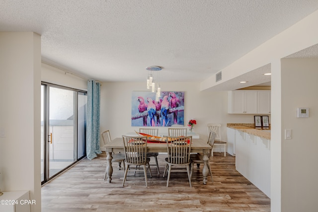 dining room with light wood-type flooring and a textured ceiling