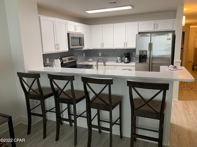 kitchen with white cabinetry, appliances with stainless steel finishes, kitchen peninsula, light wood-type flooring, and a breakfast bar