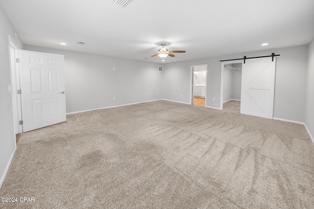 interior space with ceiling fan, a barn door, light colored carpet, and ensuite bathroom