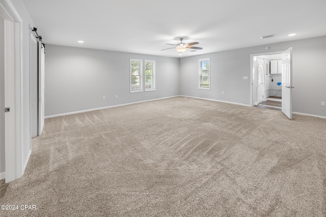 carpeted spare room with ceiling fan and a barn door