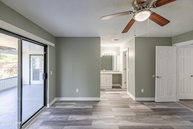 unfurnished bedroom with ensuite bathroom, a textured ceiling, access to exterior, ceiling fan, and light hardwood / wood-style flooring