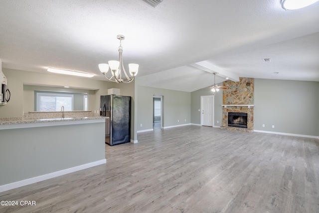 kitchen with vaulted ceiling with beams, a stone fireplace, hanging light fixtures, black fridge with ice dispenser, and light hardwood / wood-style floors