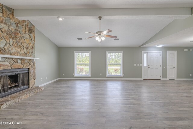 unfurnished living room with ceiling fan, lofted ceiling with beams, light hardwood / wood-style flooring, and a stone fireplace