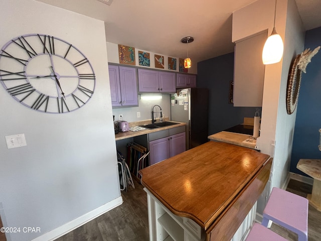 kitchen featuring a sink, baseboards, light countertops, freestanding refrigerator, and dark wood-style flooring
