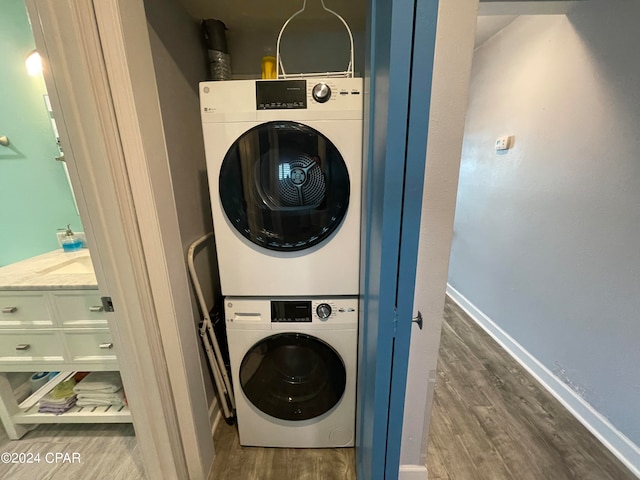 clothes washing area featuring hardwood / wood-style flooring and stacked washer / drying machine