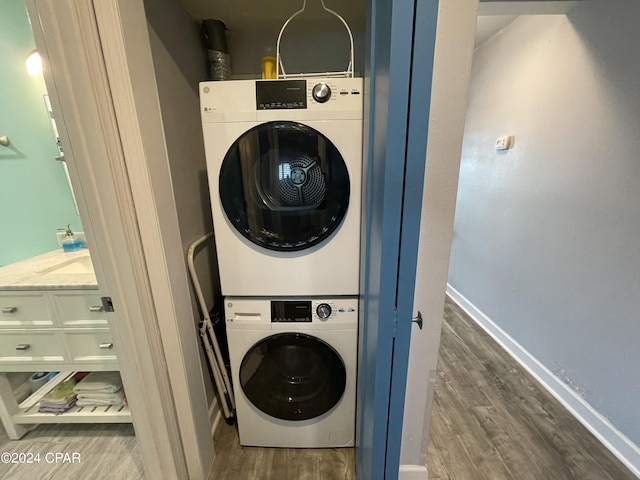 laundry room with stacked washer / dryer, laundry area, baseboards, and wood finished floors