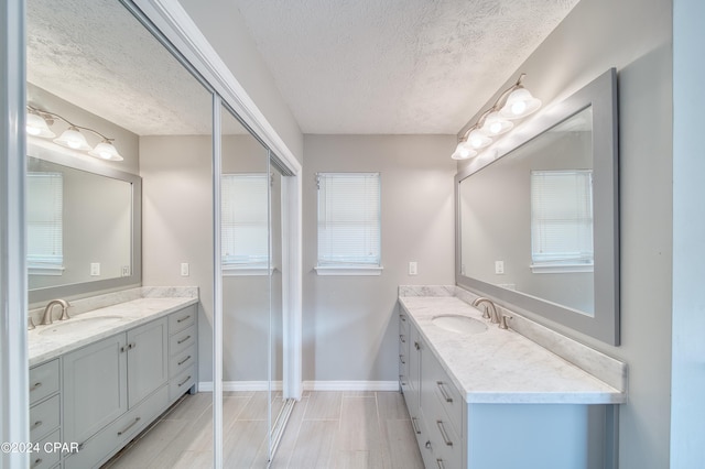 full bath with a textured ceiling, two vanities, and a sink