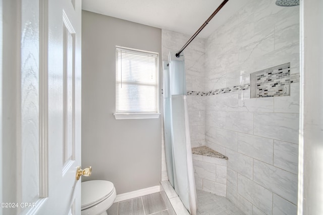 full bathroom featuring a tile shower, toilet, and baseboards