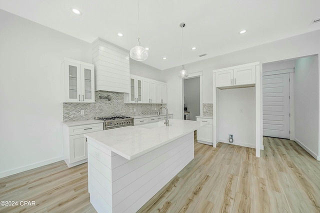 kitchen featuring white cabinetry, sink, stainless steel stove, and a center island with sink