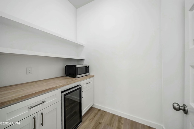 kitchen with butcher block counters, light hardwood / wood-style floors, beverage cooler, and white cabinets