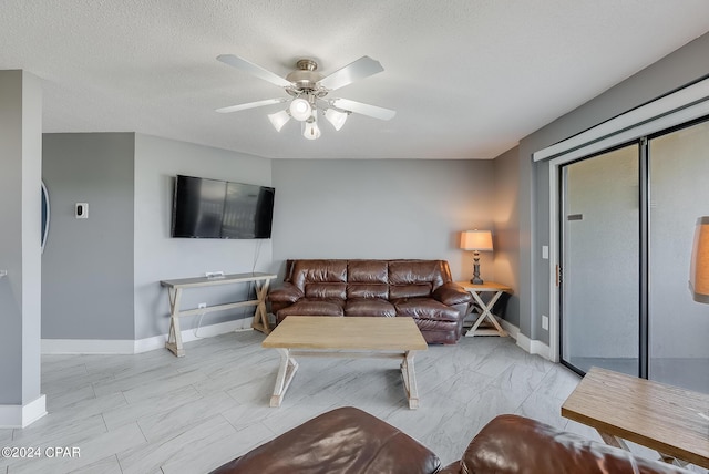 living area featuring a textured ceiling, marble finish floor, a ceiling fan, and baseboards