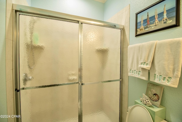 bathroom featuring toilet, a shower stall, and a textured wall