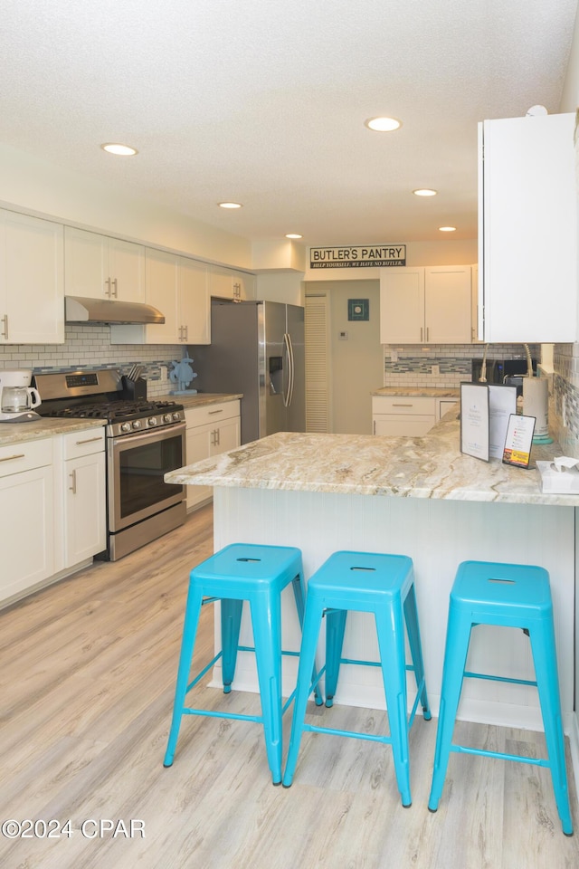 kitchen featuring light stone countertops, white cabinets, stainless steel appliances, and a breakfast bar area