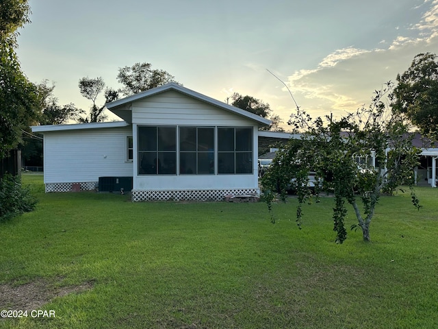 back house at dusk with a sunroom, central AC, and a yard