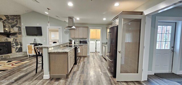 kitchen with wood-type flooring, a breakfast bar area, island exhaust hood, stainless steel appliances, and washing machine and dryer