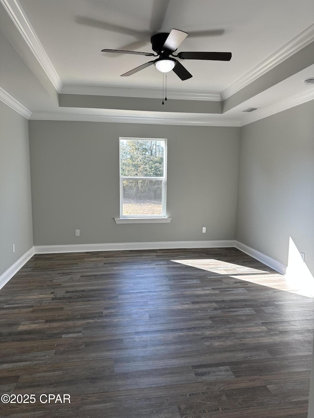 empty room with dark wood finished floors, ornamental molding, ceiling fan, baseboards, and a raised ceiling
